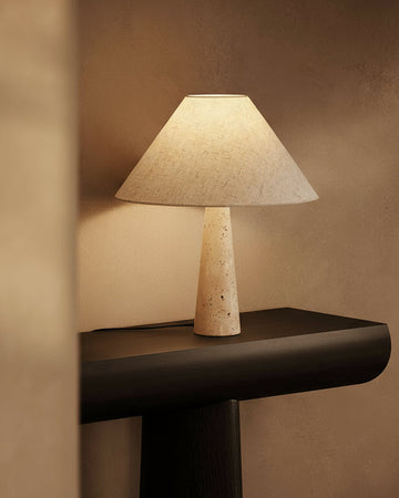 Table lamp with a textured shade on a dark surface against a beige wall