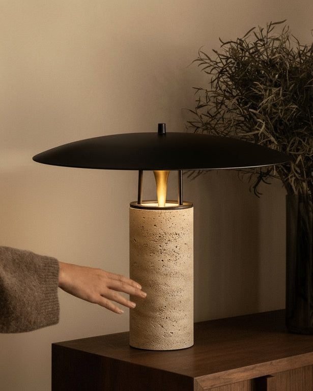 Person adjusting a modern table lamp on a wooden side table with a vase of dried plants.
